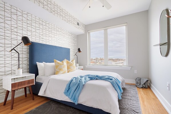 Quarto moderno com uma cama grande, vista da cidade e design geométrico na parede.