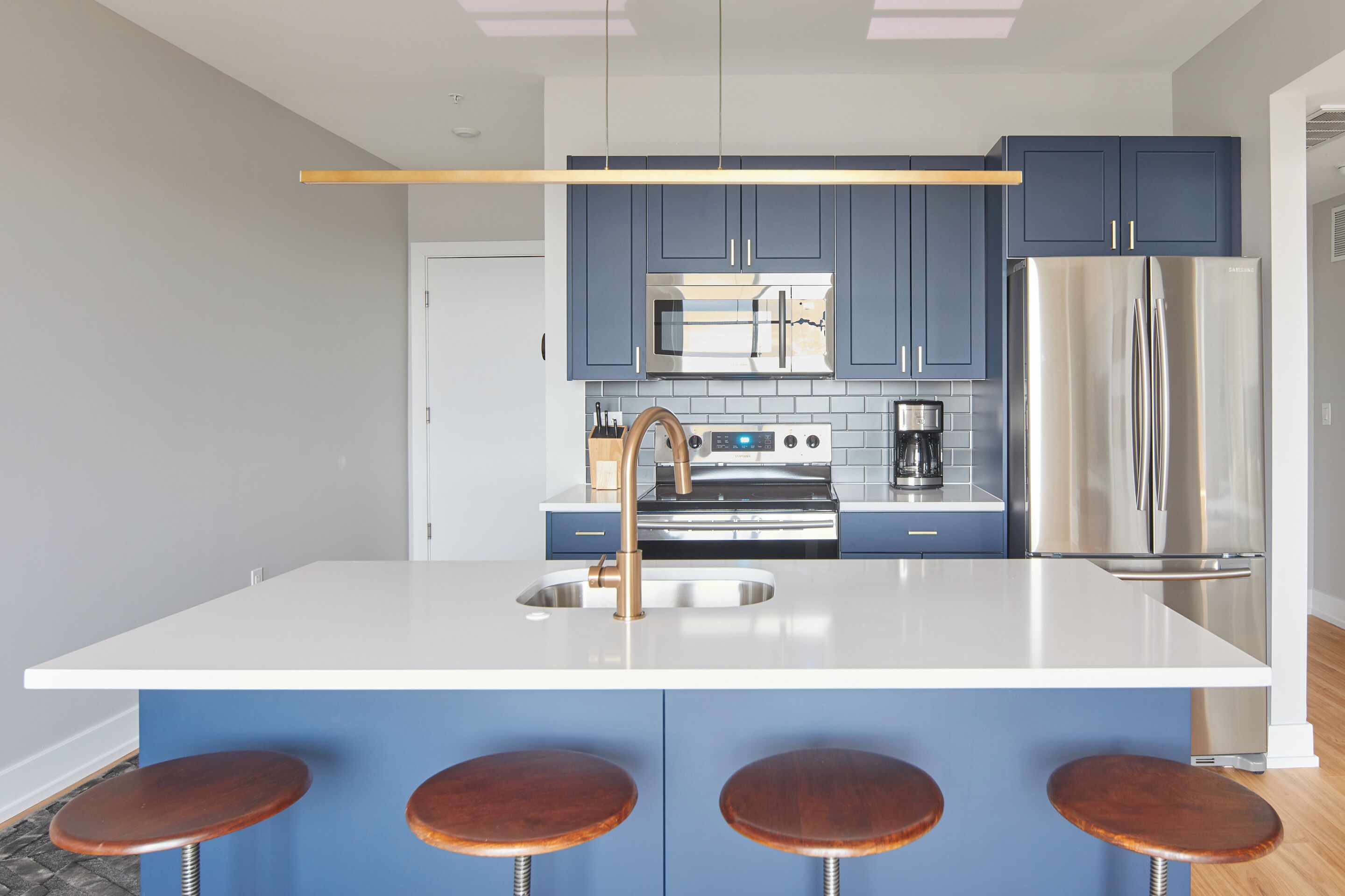 Eine moderne Küche mit blauen Schränken, einem Edelstahl-Kühlschrank, einer zentralen Kochinsel mit Hockern und einer Mikrowelle über dem Spülbecken.