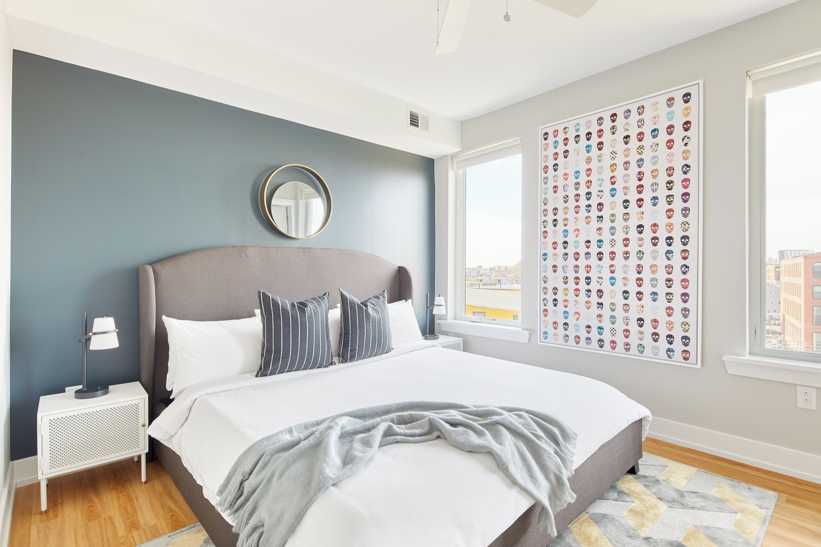 A modern bedroom with a large bed, a nightstand, a wall-mounted mirror, and a city view.