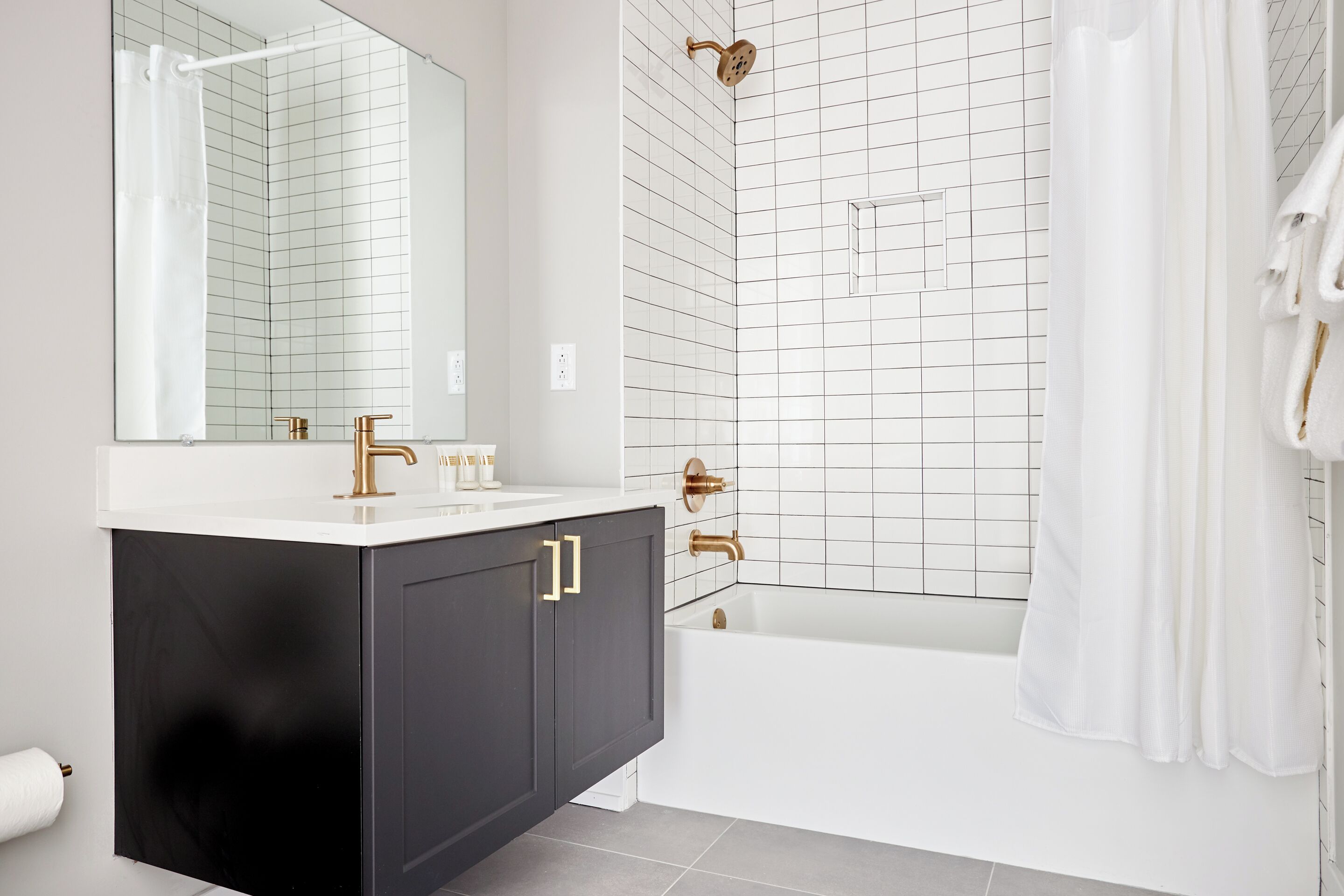 A modern bathroom with a white sink, black cabinets, a gold showerhead, and a white bathtub.