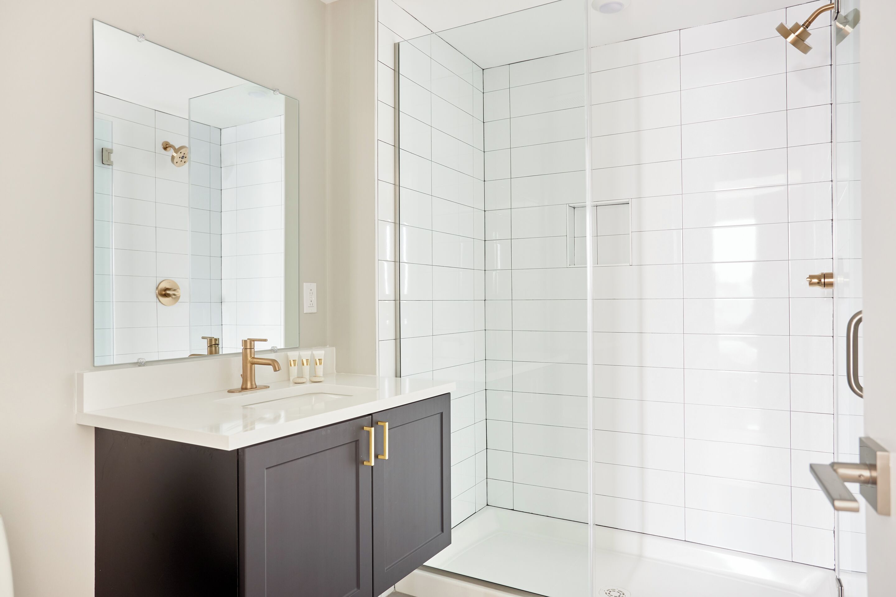 A modern bathroom with a white vanity, dark cabinets, and a glass shower enclosure.