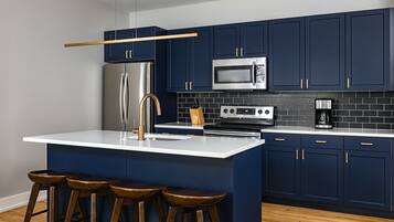 Een moderne keuken met donkerblauwe kastjes, roestvrijstalen apparatuur, een wit aanrecht en houten krukken.