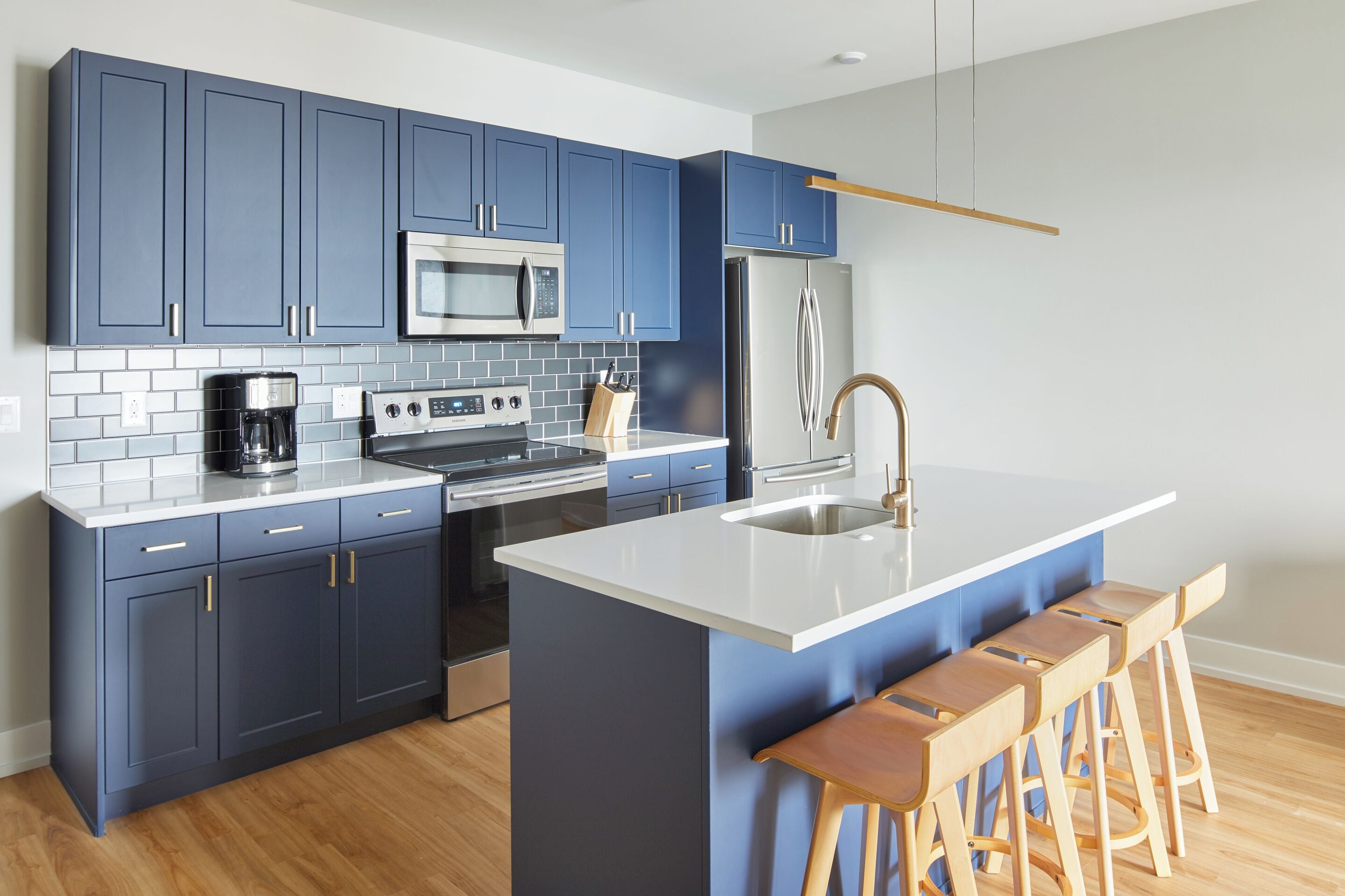 Una cocina moderna con gabinetes azules, un refrigerador de acero inoxidable, un microondas y una cafetera. Hay taburetes de madera en la isla.