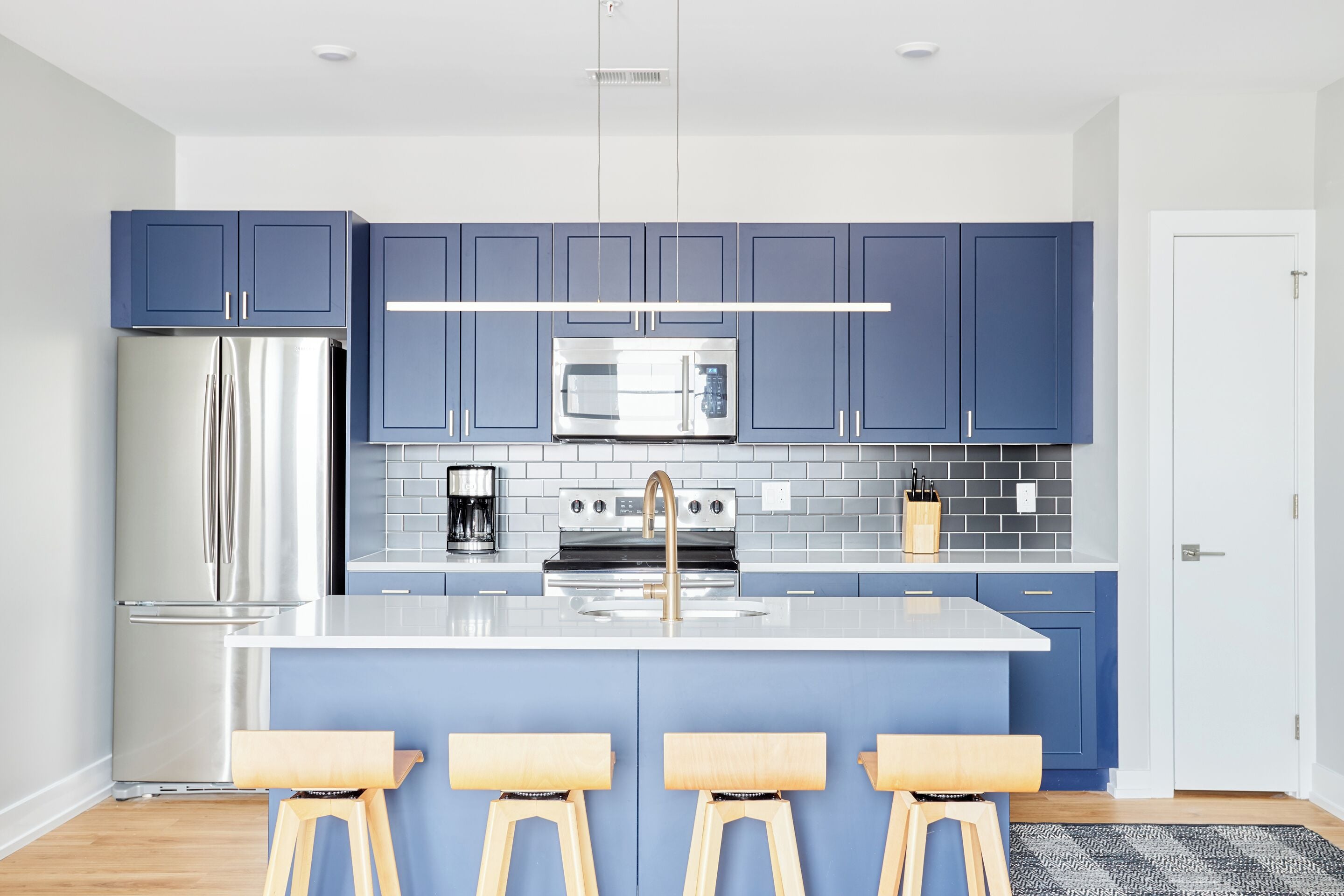 A modern kitchen with blue cabinets, stainless steel appliances, and a central island with stools.