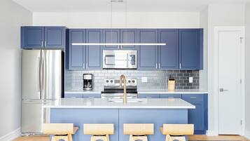 A modern kitchen with blue cabinets, stainless steel appliances, and a central island with stools.