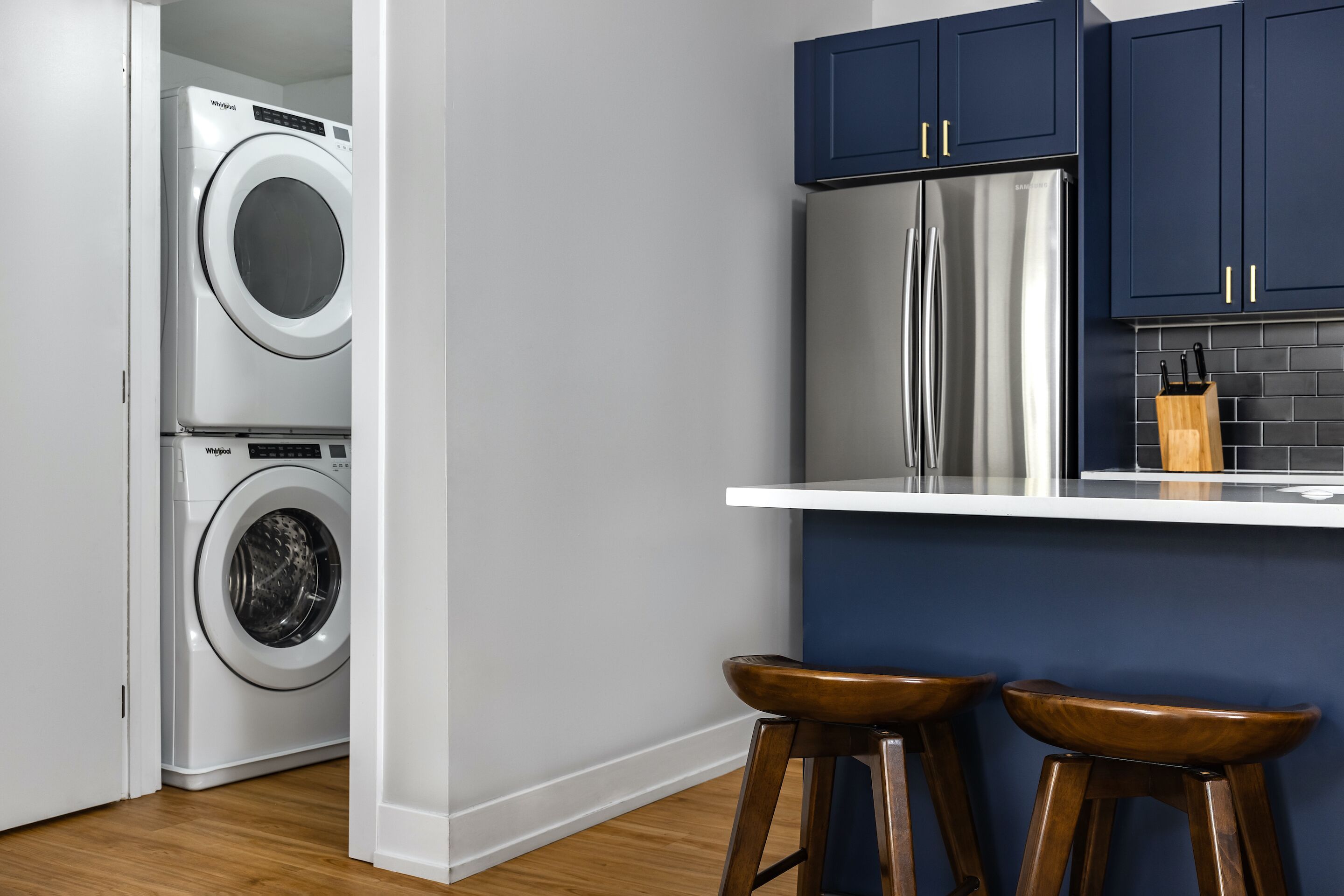 A kitchen with a washing machine, a refrigerator, and two wooden stools.
