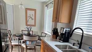 Una cucina moderna con mobili in legno, un lavello in acciaio inossidabile e una lavastoviglie. C'è un'area pranzo con tavolo e sedie, e un tappeto bianco e nero sul pavimento.