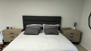 Un letto rifatto con un piumone bianco e due cuscini grigi, affiancato da due comodini in legno con cassetti.