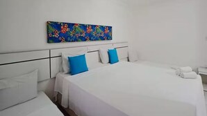 Habitación de hotel con una cama grande, dos camas más pequeñas, ropa de cama blanca, un ventilador de techo y una obra de arte colorida en la pared.