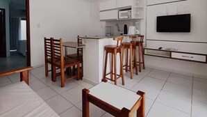 Una sala de estar moderna con comedor, cocina y televisor montado en la pared.