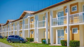 Una hilera de edificios de varios pisos en amarillo y blanco, con balcones, un coche estacionado adelante y un cielo azul despejado.