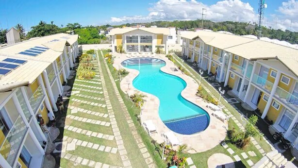 Un hotel con piscina central, varias habitaciones e un cielo despejado.