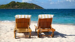 Two wooden beach chairs with striped towels on a sandy beach, overlooking a calm sea and a small island. -  
Perfect 3 bedroom family villa ,beach front view 2 minutes walk to the beach (Upper Prince's Quarter)