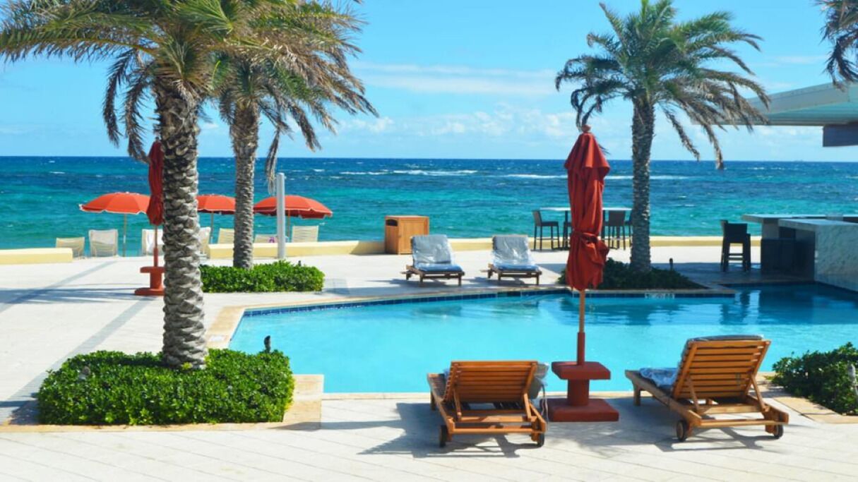 A pool area with lounge chairs, umbrellas, and palm trees.