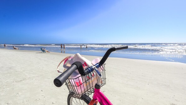 A beach scene with a bicycle and a shopping bag in the foreground. - MyStay at 1102 Sea Crest - Sea Crest Resort Oceanfront Complex | Steps to Beach (Hilton Head Island)