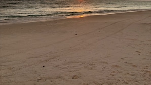 Una playa con un atardecer, olas y cielo nublado.