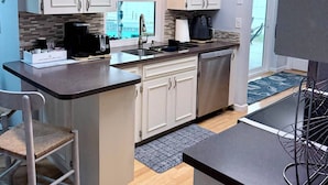 Una cocina moderna con gabinetes blancos, una isla central, electrodomésticos de acero inoxidable y vistas al exterior.