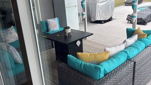 Un espacio de estar al aire libre techado con mesa, asientos acolchados, un refrigerador y una piscina cubierta.