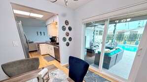Una sala de estar moderna con comedor, una cocina al fondo y vista a un área de piscina exterior.