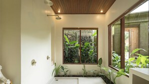 A bathroom with a shower, a sink, and a window with plants. - Villa Celagi (Ubud)