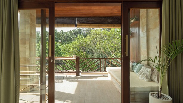A balcony with a wooden railing, a potted plant, and a view of lush greenery. - Villa Celagi (Ubud)