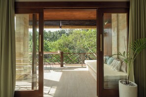 Een balkon met een houten leuning, een bloempot en uitzicht op weelderige begroeiing.
