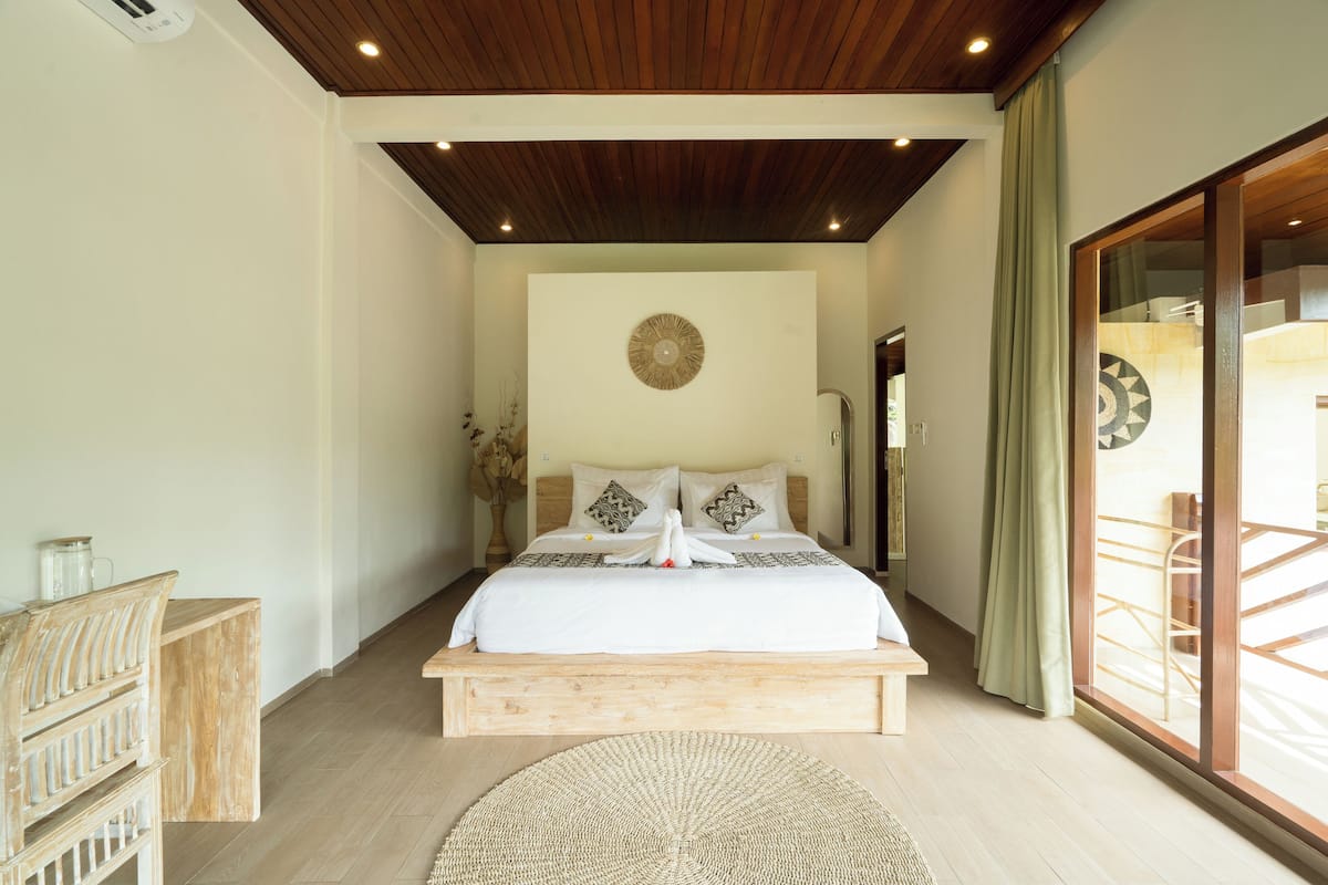 A bedroom with a wooden bed frame, a large round rug, and a view of the outside through a sliding glass door.