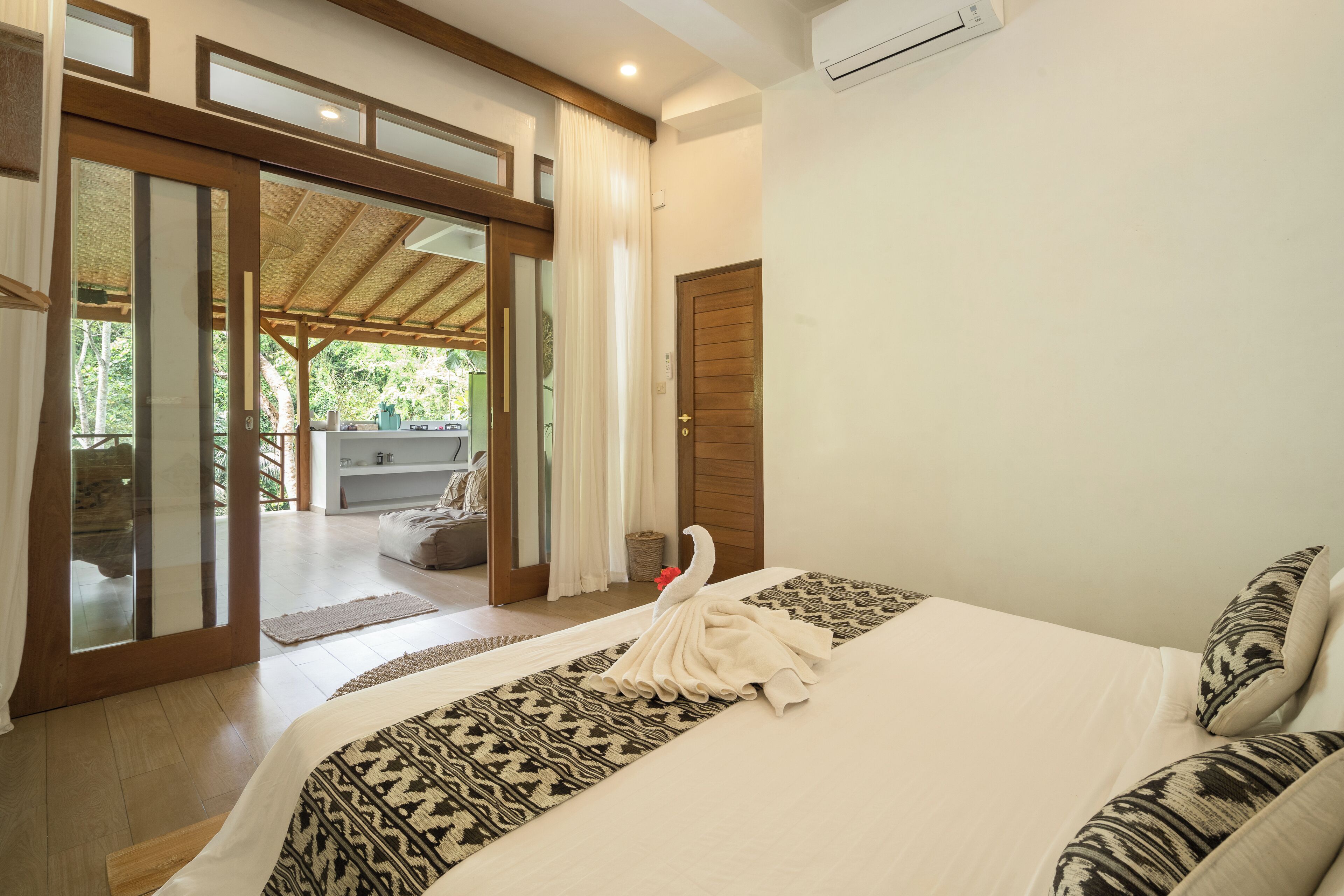 A hotel room with a large bed, a wooden door, and a view of an outdoor area with a covered seating area.