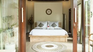 A bedroom with a wooden bed, white bedding, and a decorative wall piece. - Villa Celagi (Ubud)