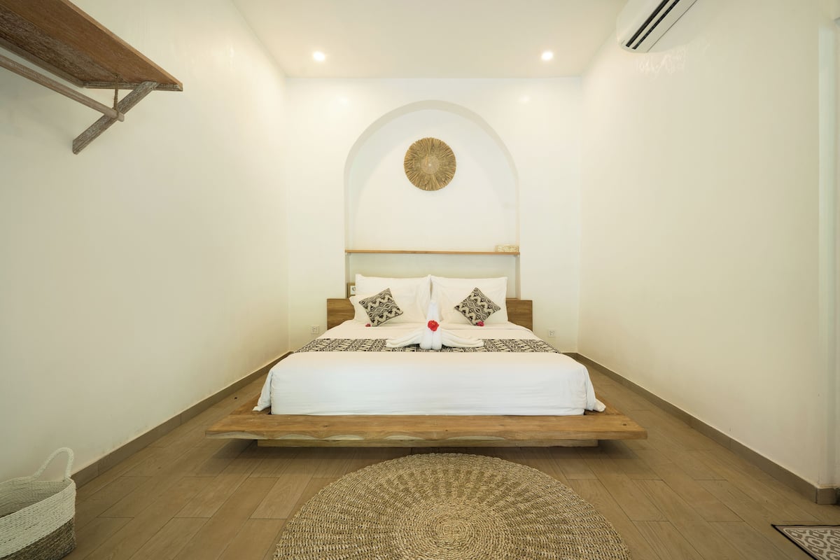 A bedroom with a wooden platform bed, white bedding, and a decorative wall piece above the bed.