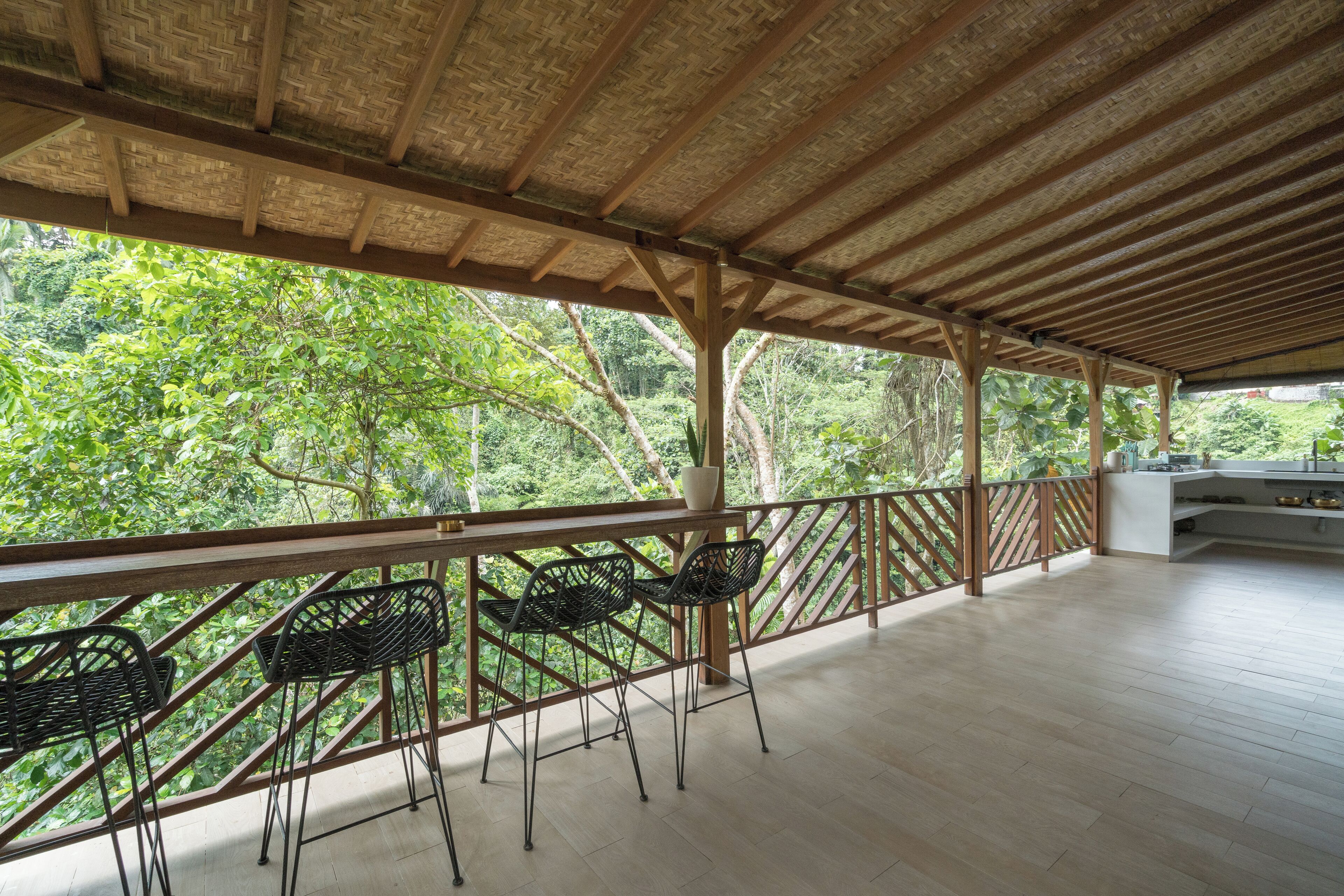 Une terrasse extérieure dotée d’un plafond en bois et d’une balustrade offrant une vue sur une végétation luxuriante.
