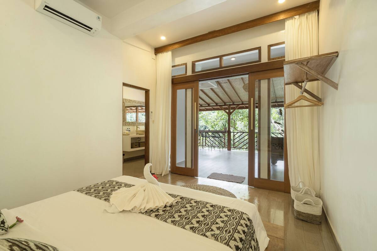 A hotel room with a bed, a hanging coat rack, and a view of the outdoor area.