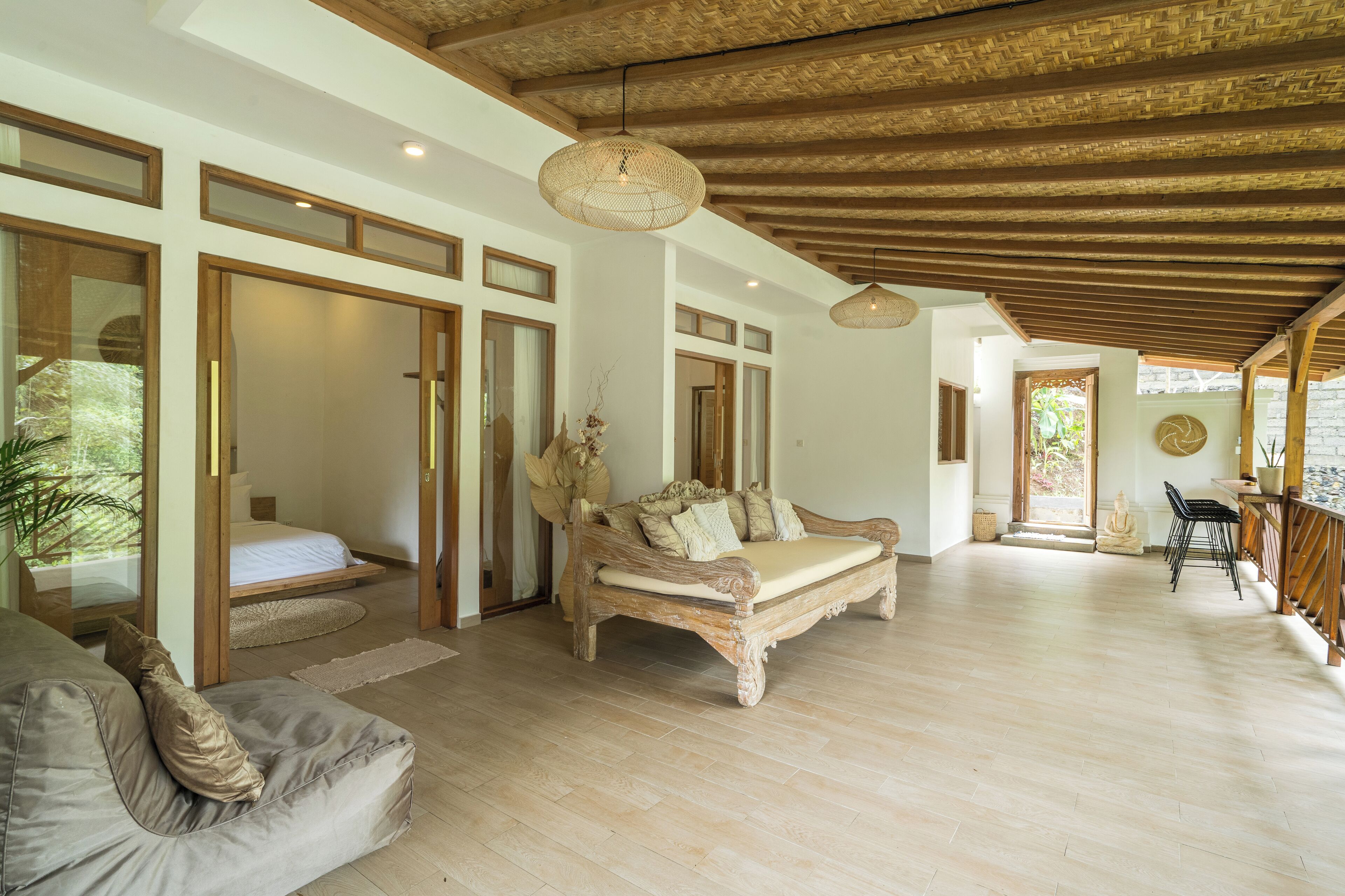 A spacious room with a large bed, a sofa, and a wooden ceiling. There is a window and a door leading to another room.