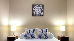 A neatly made bed with white bedding and two decorative pillows with a floral design. There are two bedside lamps on wooden nightstands, and a piece of abstract art hangs on the wall above the bed. - Casa Florencia Liberia (Liberia)