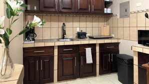 A kitchen with dark wooden cabinets, a tiled backsplash, a sink, a stove, and a trash can. - Casa Florencia Liberia (Liberia)