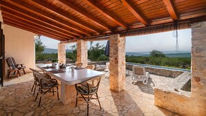 An outdoor patio with stone flooring, a table set for dining, and stone pillars.