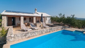 A house with a swimming pool, stone walls, and a solar panel on the roof.