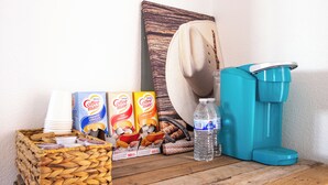 Una estación de café con cafetera, vasos desechables, leche para café y una botella de agua.