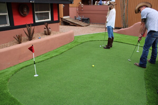 Campo de golf con una bandera roja, una pelota y dos personas jugando.