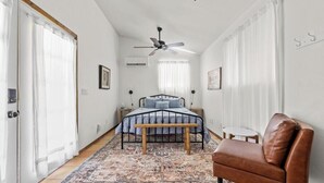 Un dormitorio con una cama, un sillón de cuero marrón, una mesita redonda y un ventilador de techo.