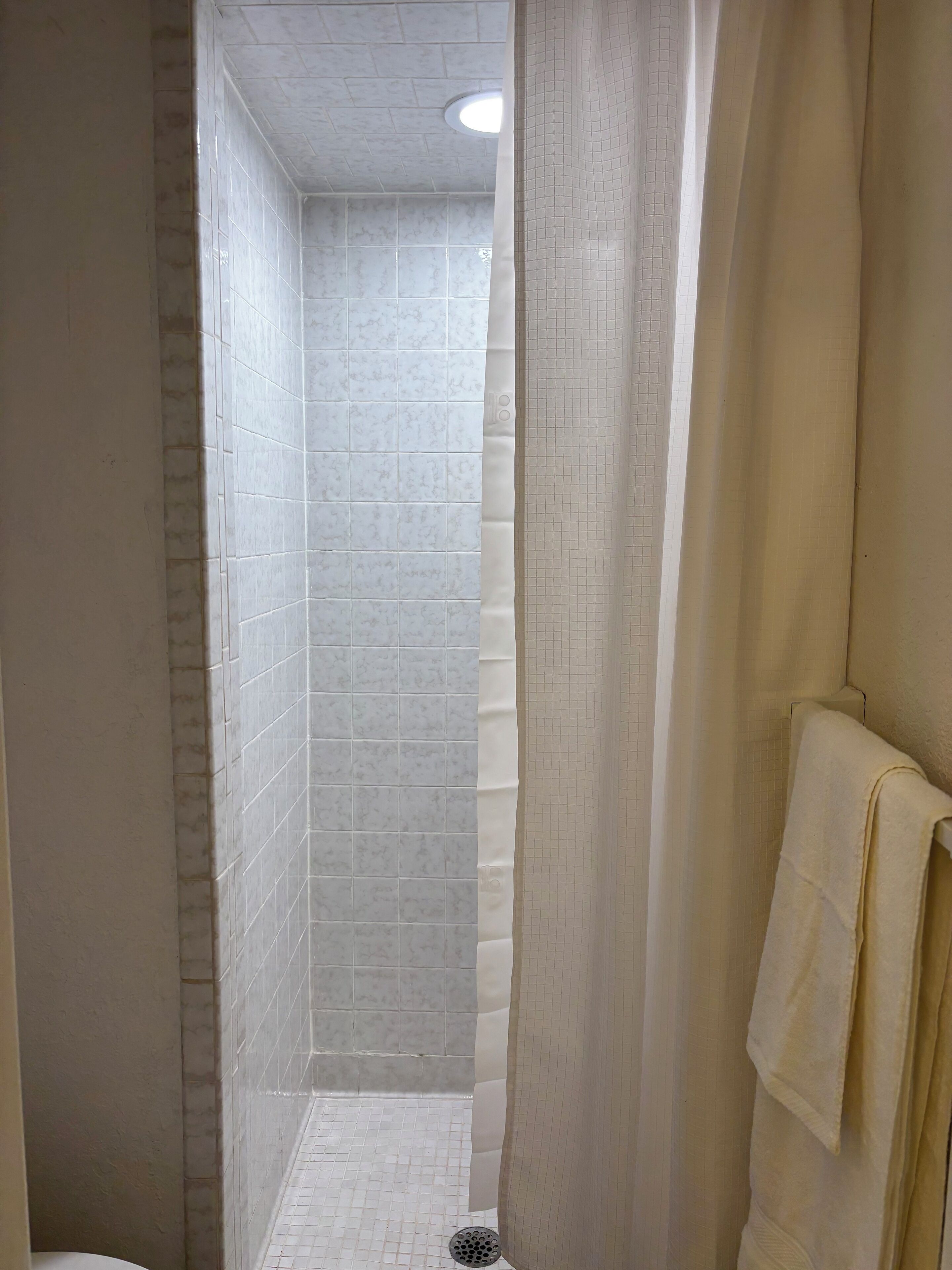 Un petit espace douche aux murs carrelés et doté d’un luminaire au plafond.
