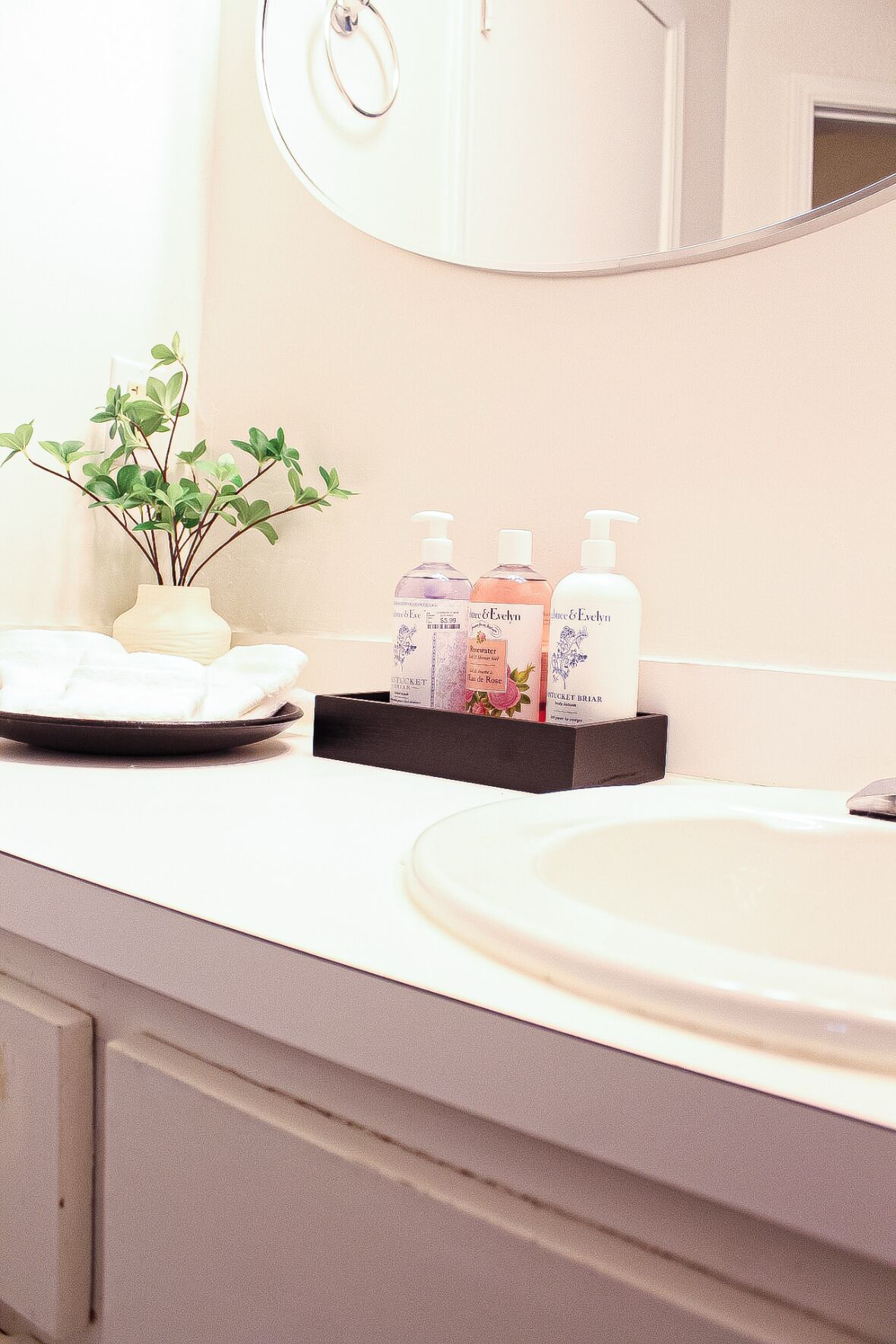 A bathroom with a white sink, a mirror, and toiletries on a tray.