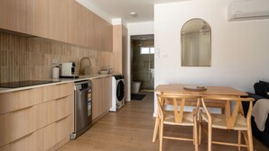 A modern kitchen with wooden cabinets, a dishwasher, and a washing machine. There is a wooden dining table with chairs.