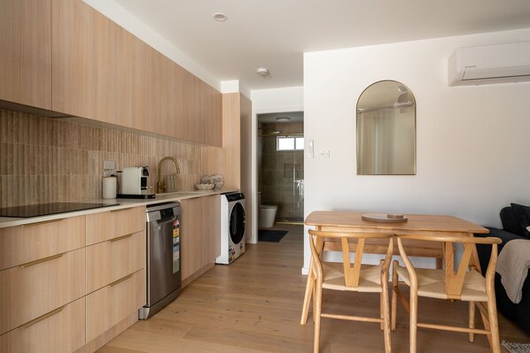 A modern kitchen with wooden cabinets, a dishwasher, and a washing machine. There is a wooden dining table with chairs.