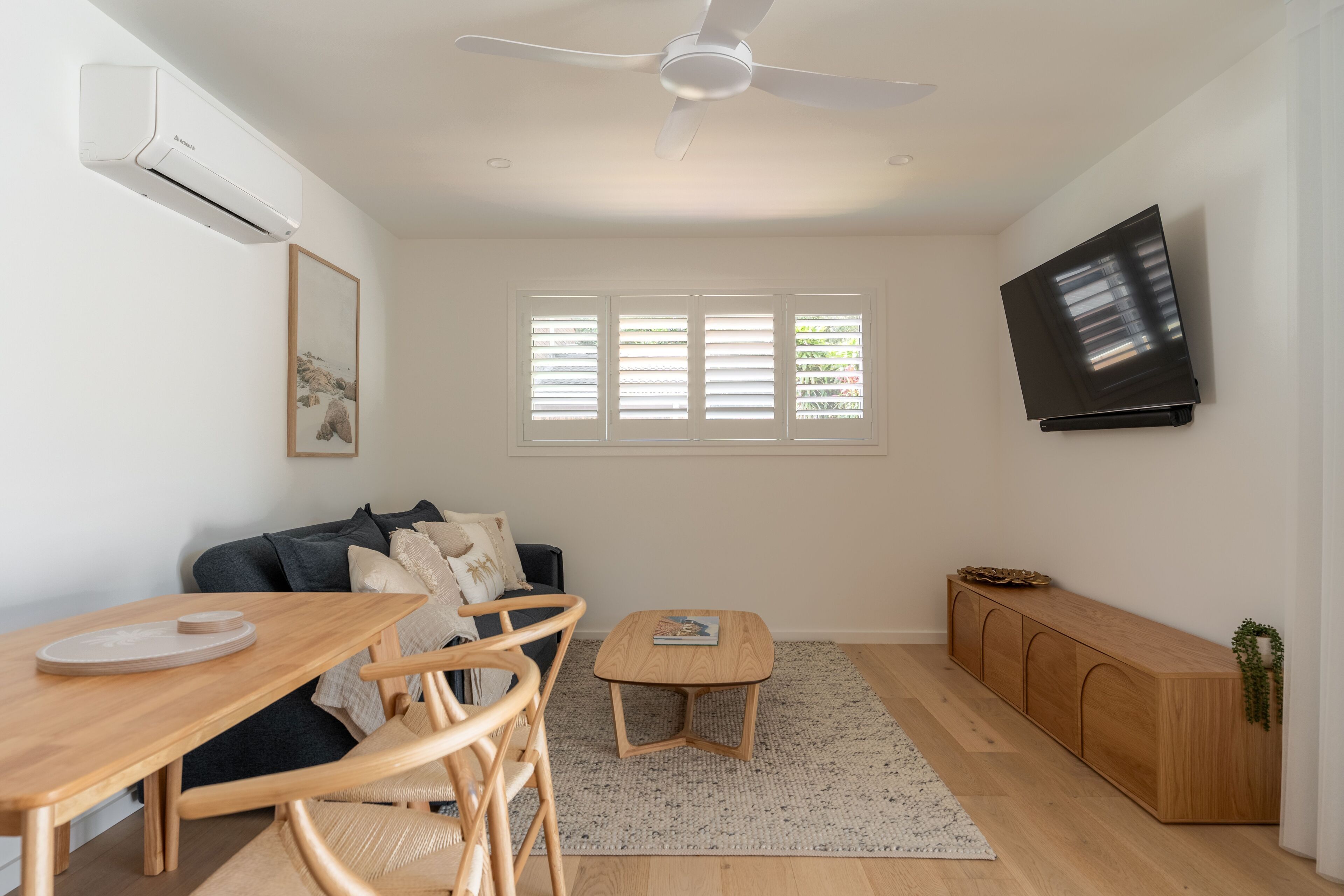 Een moderne woonkamer met een plafondventilator, een flatscreen televisie, een bank, een houten eettafel en een bijzettafeltje.