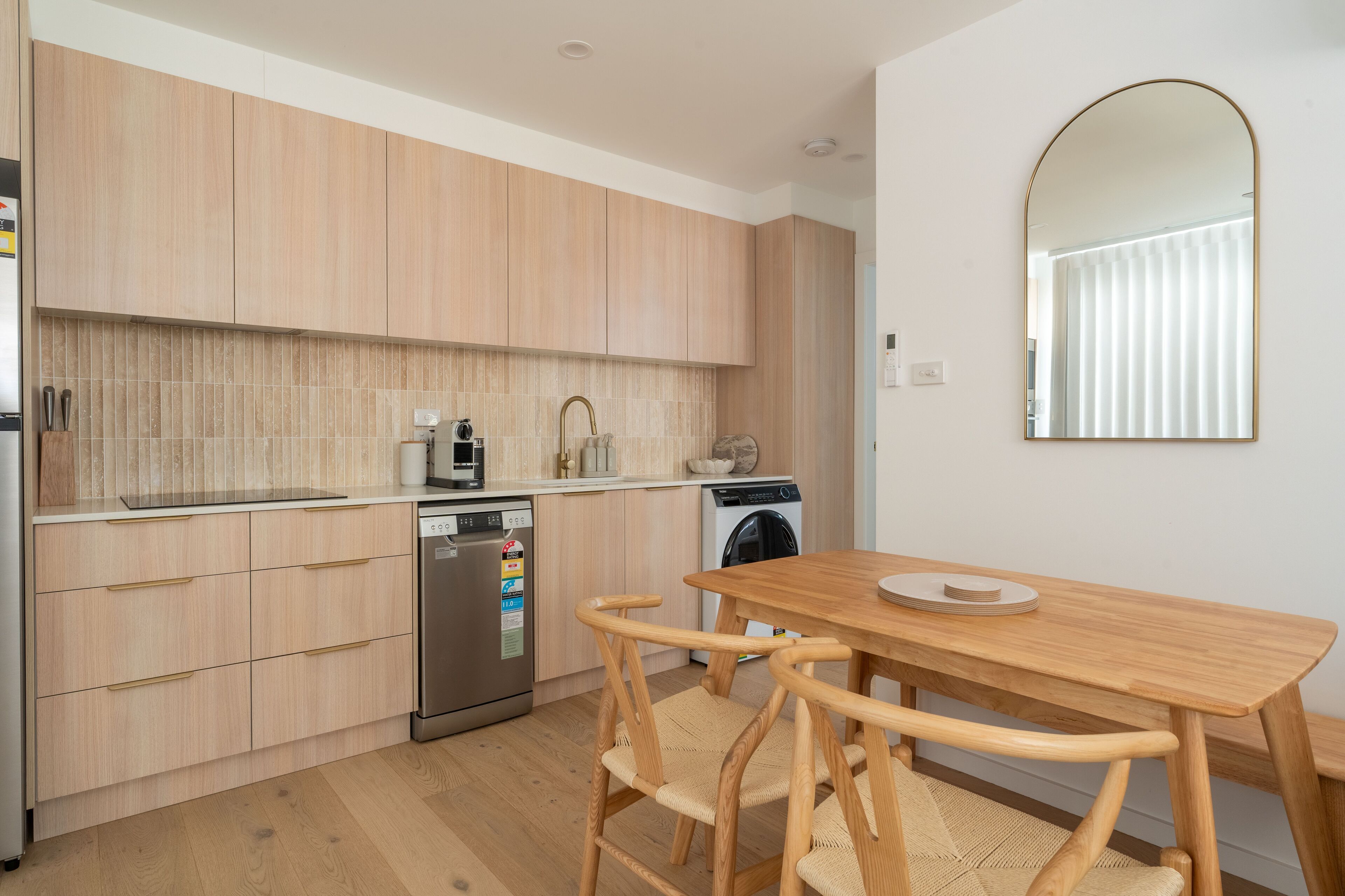 A modern kitchen with wooden cabinets, a dishwasher, a washing machine, and a dining area with a wooden table and chairs.