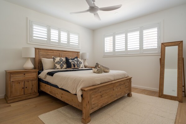 Une chambre à coucher avec un lit en bois, deux tables de chevet, un ventilateur de plafond et un grand miroir.