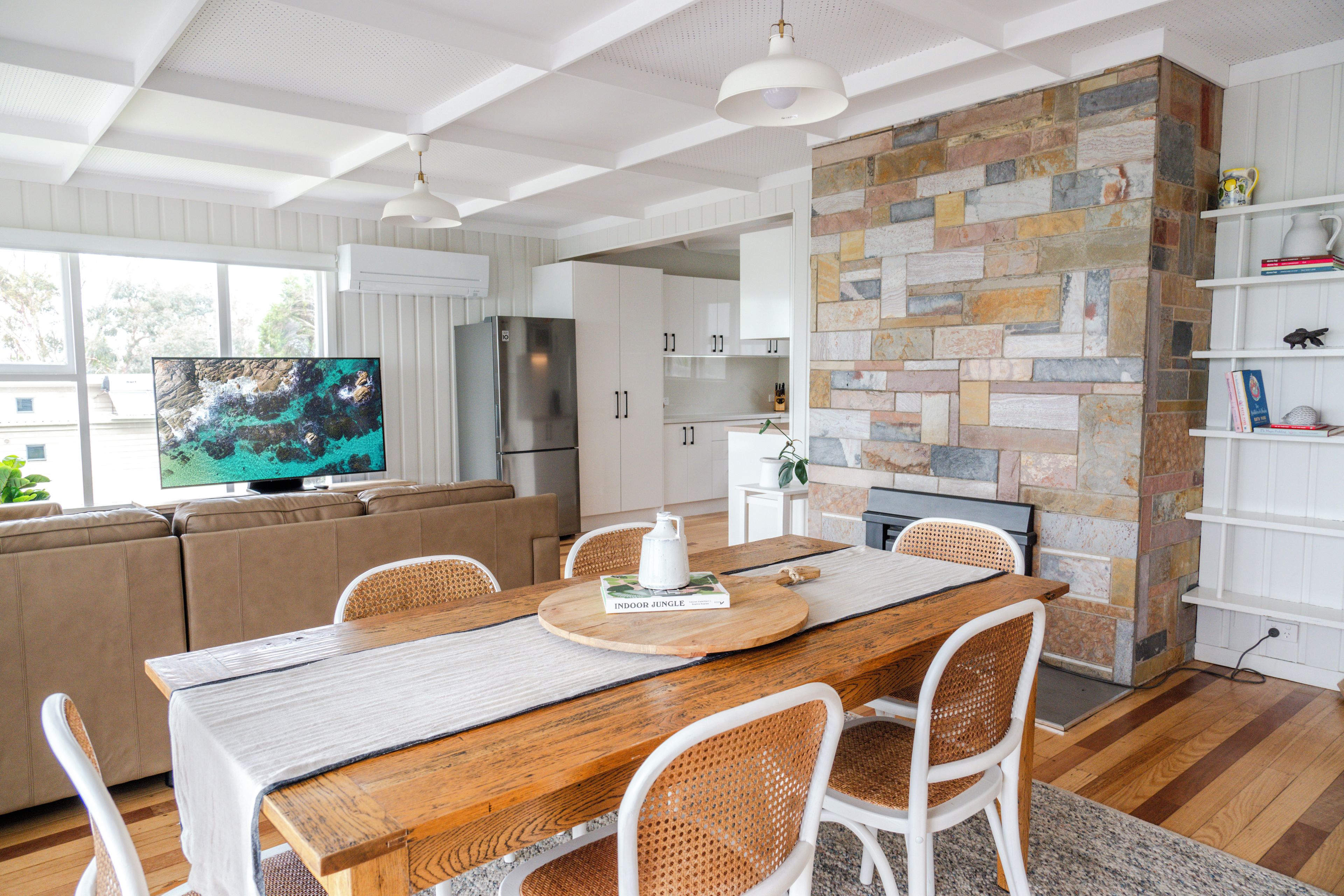 A modern kitchen with a stone wall, wooden dining table, and white cabinetry.