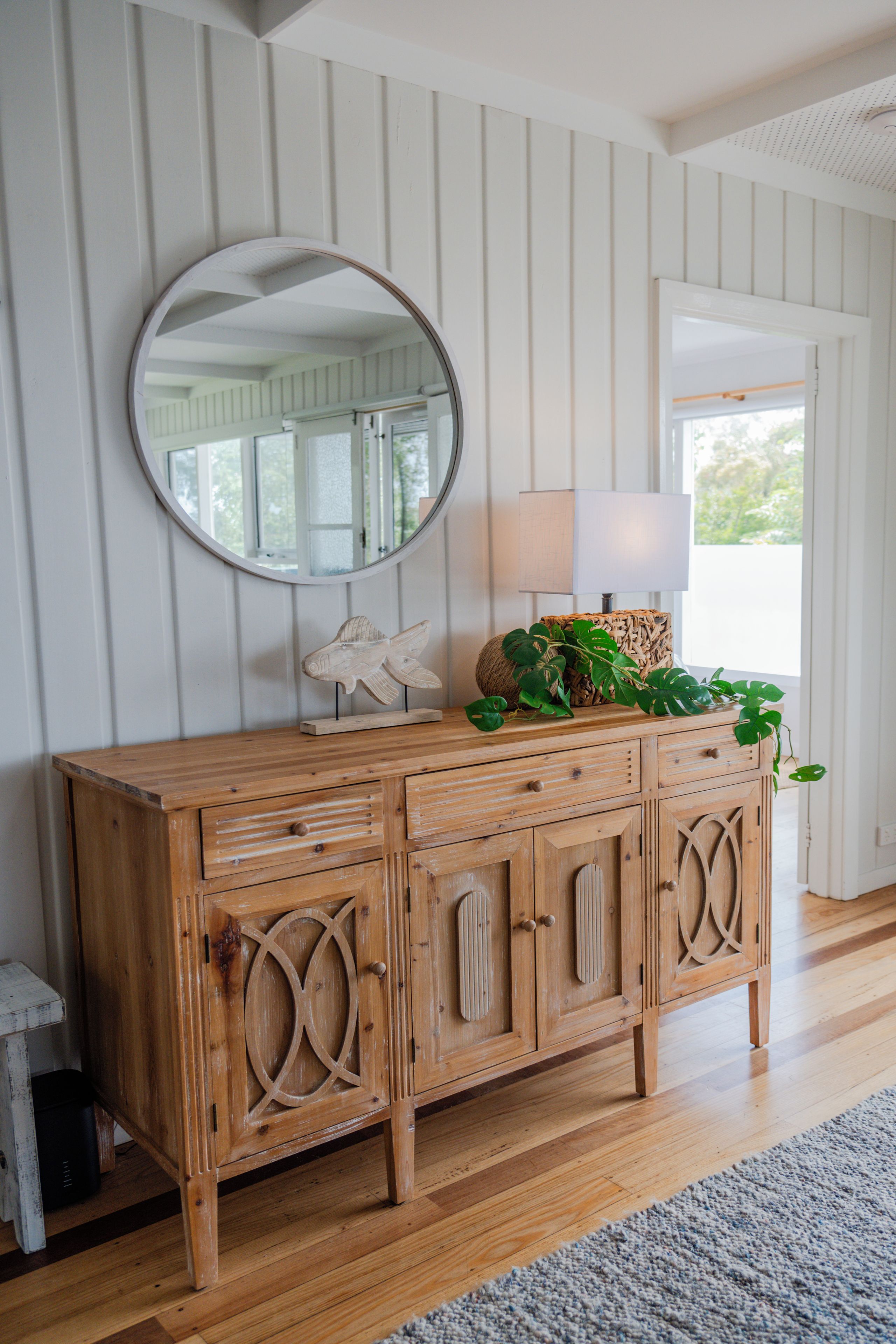 A wooden dresser with a round mirror, a lamp, and decorative items.