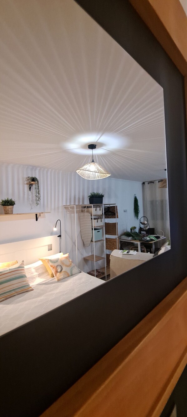 Quarto com cama, mesa de cabeceira, abajur e um espelho refletindo o ambiente.